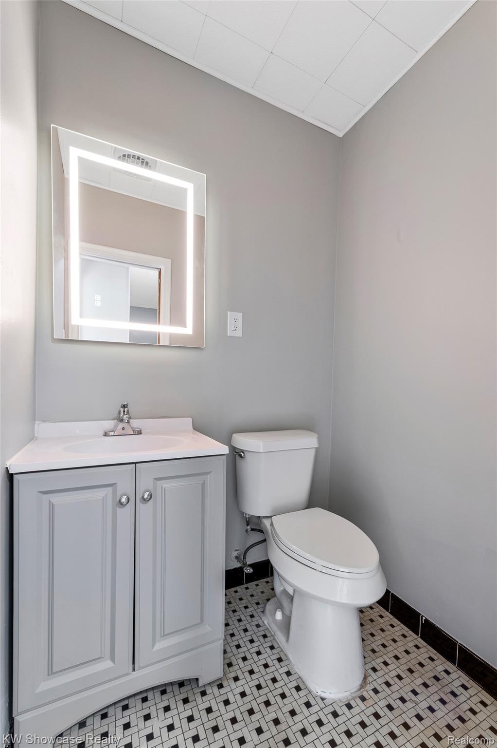 8936 Merriman Road Livonia, MI 48150 - Photo 37 of 49 Bathroom featuring an illuminated vanity mirror, a gray cabinet vanity with integrated sink, and black and white geometric floor tiling