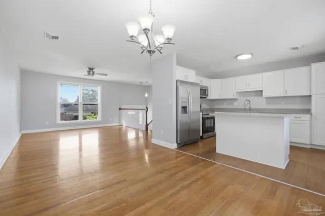 a kitchen with stainless steel appliances granite countertop a refrigerator a sink dishwasher a stove and white cabinets with wooden floor