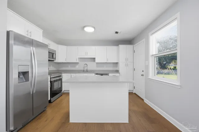 a kitchen with stainless steel appliances granite countertop a refrigerator a sink dishwasher a stove and white countertops with wooden floor