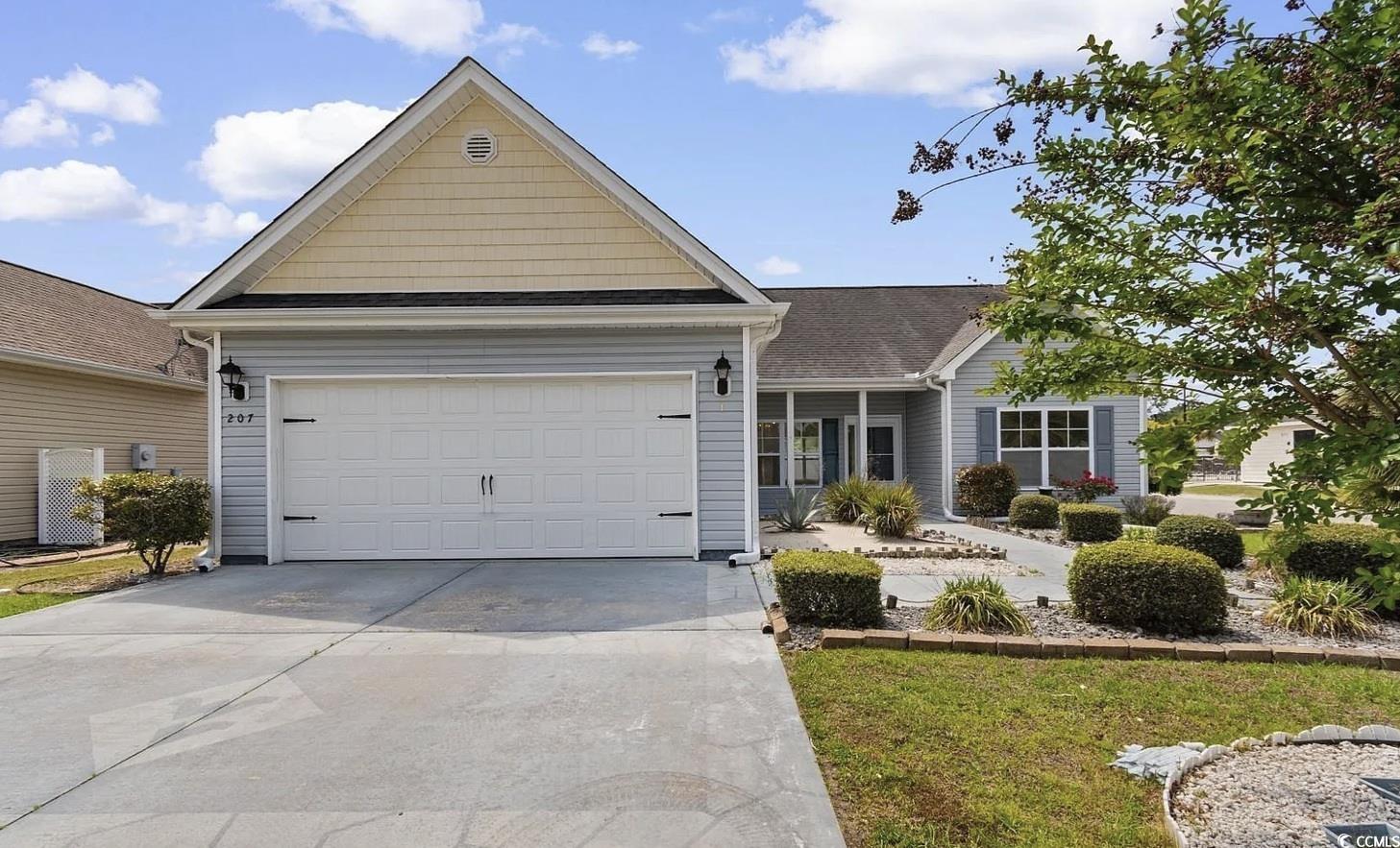 View of front of home featuring a porch, driveway, an attached garage, roof with shingles, and a front yard