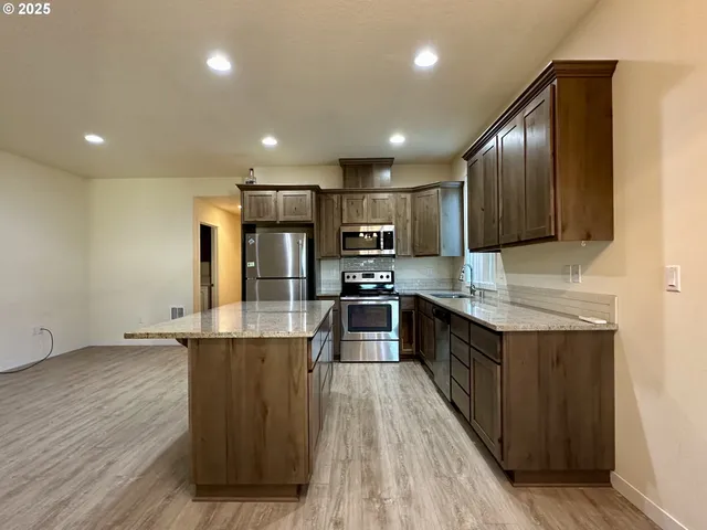 a kitchen with stainless steel appliances granite countertop wooden cabinets a sink dishwasher a stove and a refrigerator