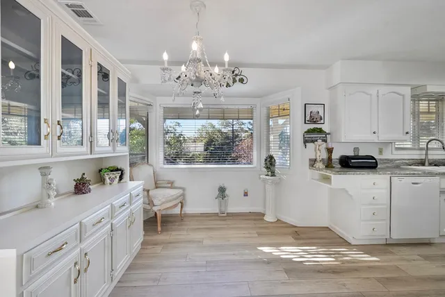 a large white kitchen with stainless steel appliances kitchen island granite countertop a stove a sink a refrigerator and white cabinets with wooden floor