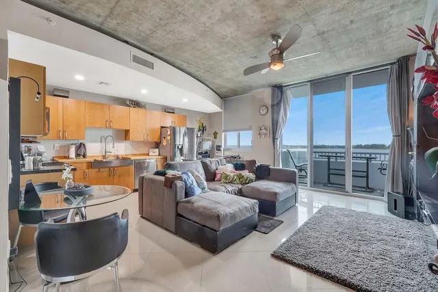 a living room with furniture potted plant kitchen view and a large window