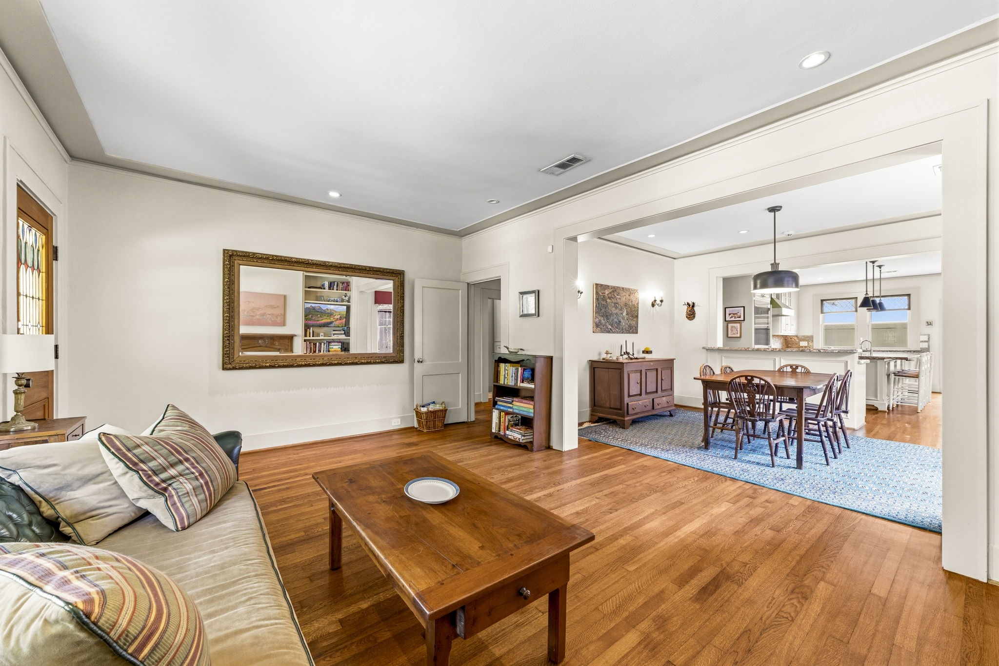 1521 Kipling Street Houston, TX 77006 - Photo 11 of 35 This photo showcases a bright, open-concept living and dining area with hardwood floors. The living room features a cozy sofa and coffee table, while the dining area includes a wooden table and chairs under modern lighting. The space is inviting and well-lit, with a view into the kitchen.