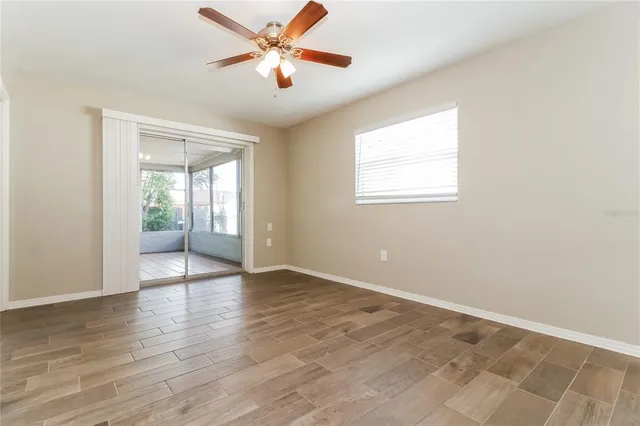 an empty room with wooden floor chandelier fan and windows