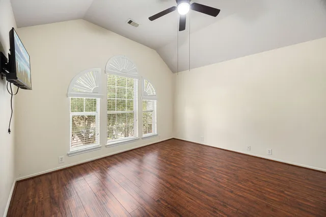 an empty room with wooden floor fan and windows