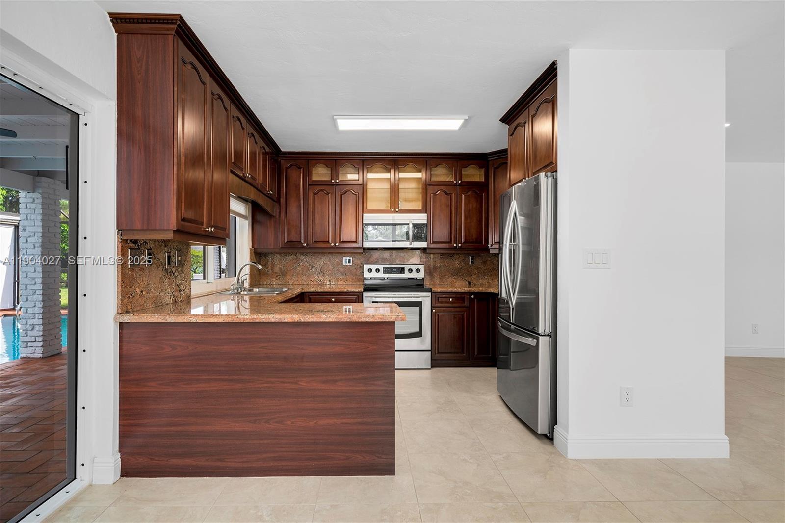7575 Southwest 134th Street Pinecrest, FL 33156 - Photo 6 of 28 a kitchen with stainless steel appliances granite countertop a refrigerator a stove and a sink with wooden cabinets