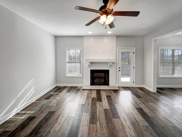 an empty room with windows a fireplace a ceiling fan and wooden floor
