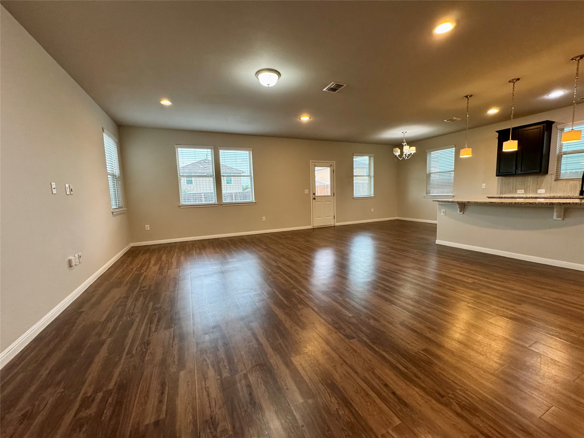 219 Wapiti Road Buda, TX 78610 - Photo 3 of 24 Unfurnished living room with dark wood-type flooring, suspended lighting, and plenty of natural light