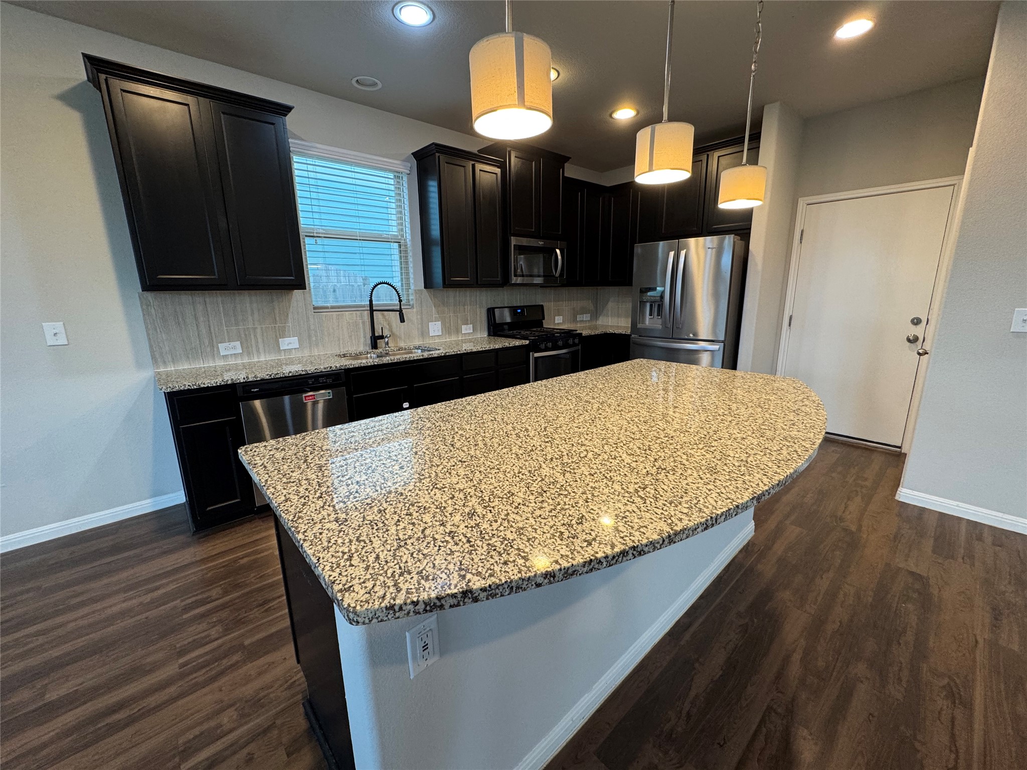 219 Wapiti Road Buda, TX 78610 - Photo 9 of 24 Kitchen with stainless steel appliances, a kitchen island, light stone counters, decorative light fixtures, and dark wood finished floors