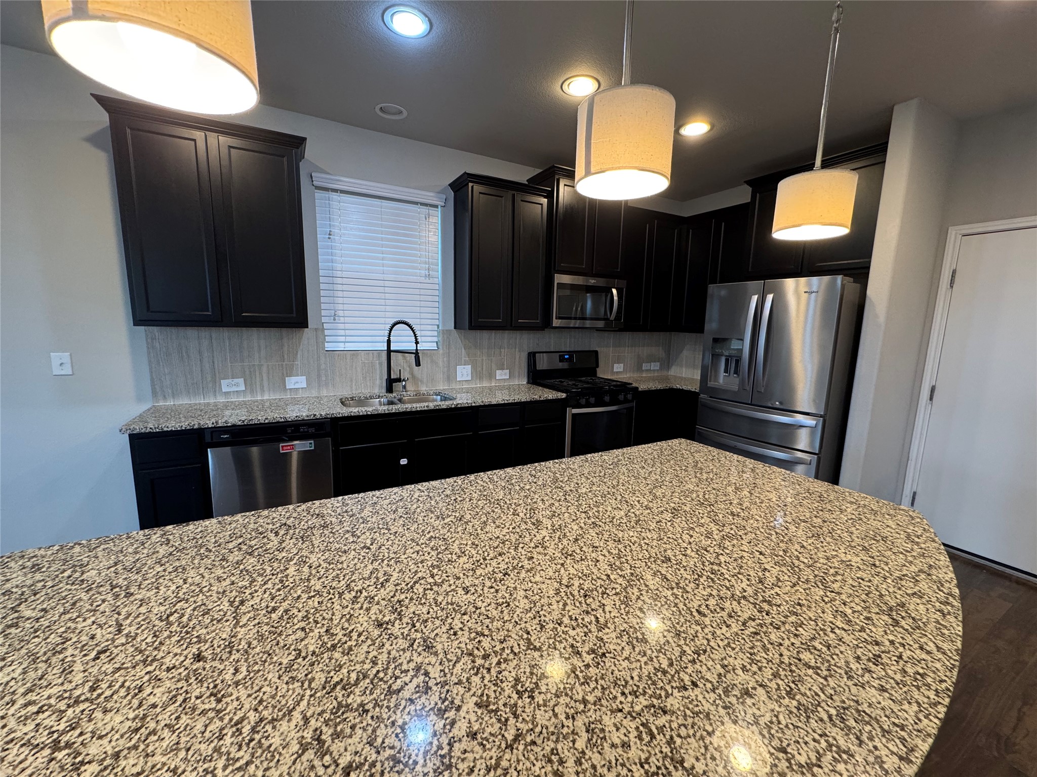 219 Wapiti Road Buda, TX 78610 - Photo 10 of 24 Kitchen with stainless steel appliances, decorative backsplash, light stone countertops, and decorative light fixtures