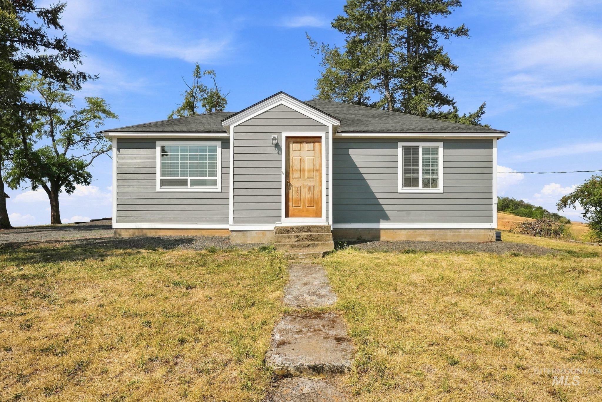 16078 Hoffman Road Kendrick, ID 83537 - Photo 1 of 47 Gray siding exterior with white trim, wood-finish entry door, and multi-pane windows
