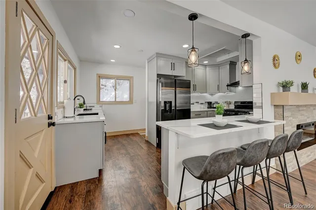 a kitchen view with stainless steel appliances kitchen island granite countertop a refrigerator a stove top oven a sink dishwasher and white cabinets with wooden floor