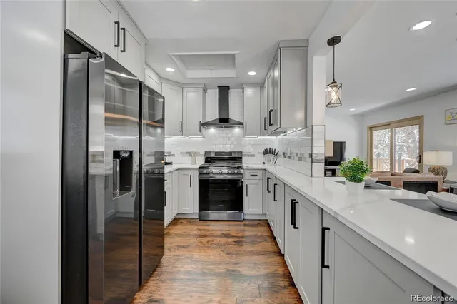 a kitchen with stainless steel appliances granite countertop a refrigerator a sink dishwasher a stove and white cabinets with wooden floor