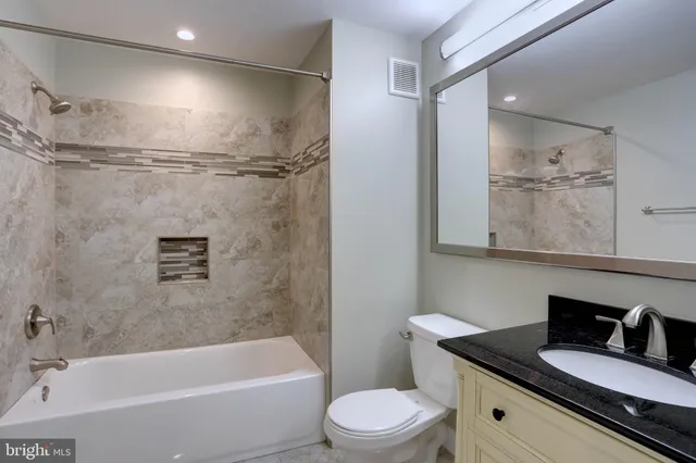 a bathroom with a granite countertop bathtub shower sink vanity and toilet