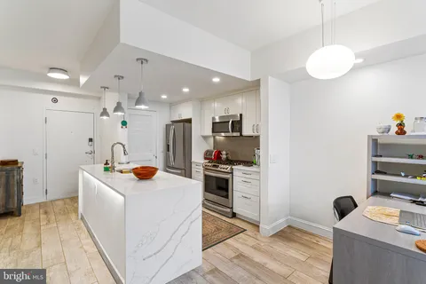 a large white kitchen with a stove a sink a refrigerator and a dining table with wooden floor