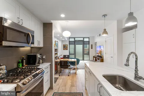 a kitchen with stainless steel appliances a stove a sink a microwave a dining table and chairs with wooden floor