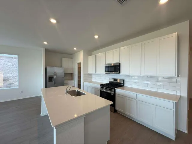 a view of an empty room with kitchen view and appliances