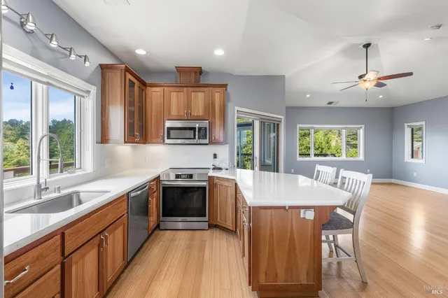 a open kitchen with stainless steel appliances granite countertop a stove top oven a sink dishwasher a dining table and chairs with wooden floor