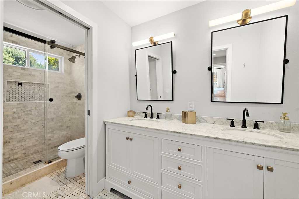 8741 La Roca Avenue Fountain Valley, CA 92708 - Photo 25 of 50 Primary bath with dual sinks, quartz countertop, and a pocket door to the walk-in shower with clear glass barn door style enclosure and designer tile surround
