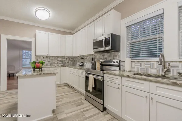 a kitchen with granite countertop a sink stainless steel appliances and white cabinets