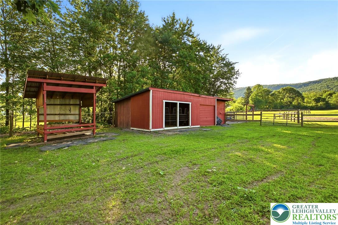 9033 Loop Road Slatington, PA 18080 - Photo 46 of 53 A vibrant red barn and open-air feeder stand ready for livestock in a lush, fenced pasture.