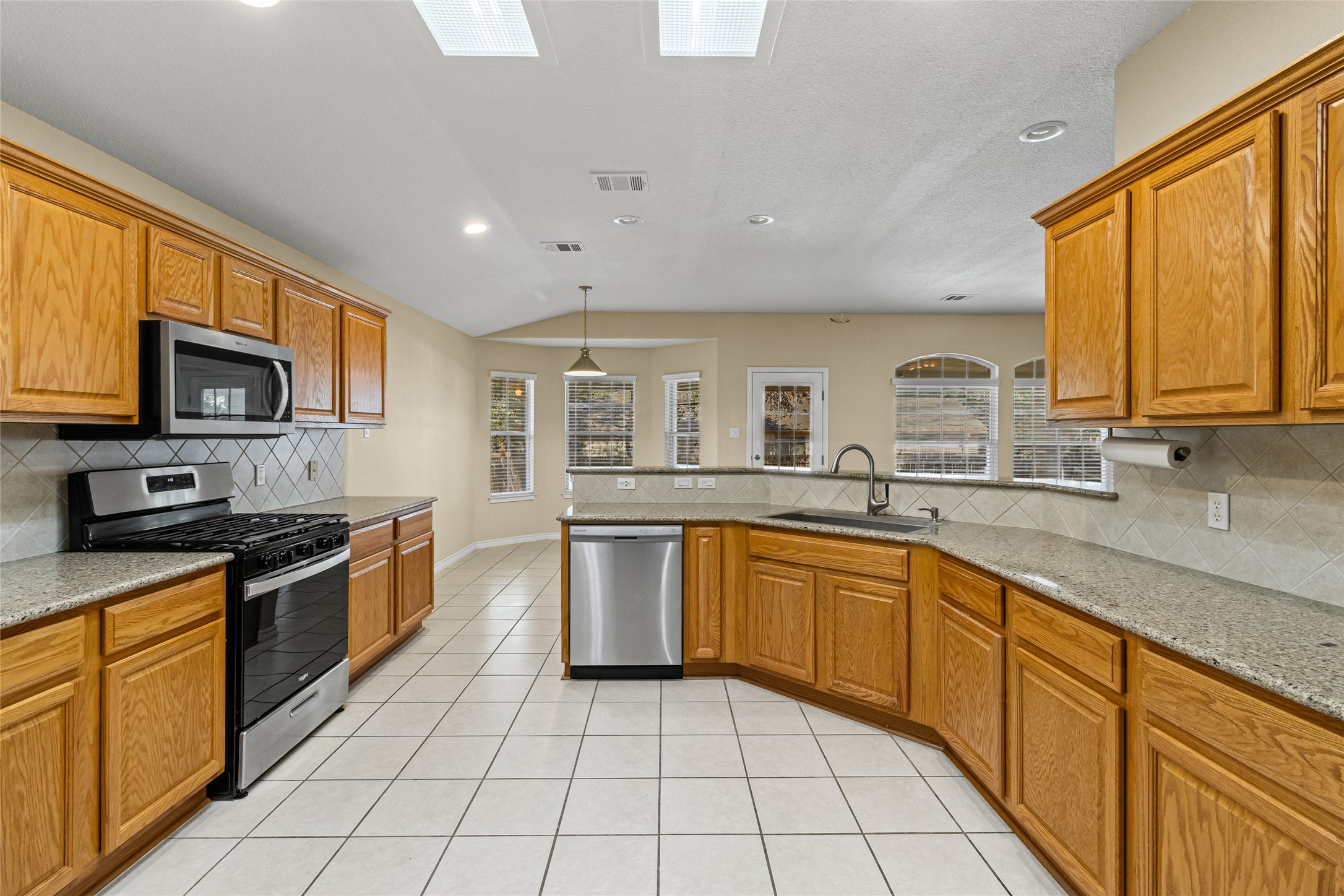 14901 Staked Plains Loop Austin, TX 78717 - Photo 11 of 30 Kitchen featuring backsplash, stainless steel appliances, brown cabinetry, light stone countertops, and recessed lighting