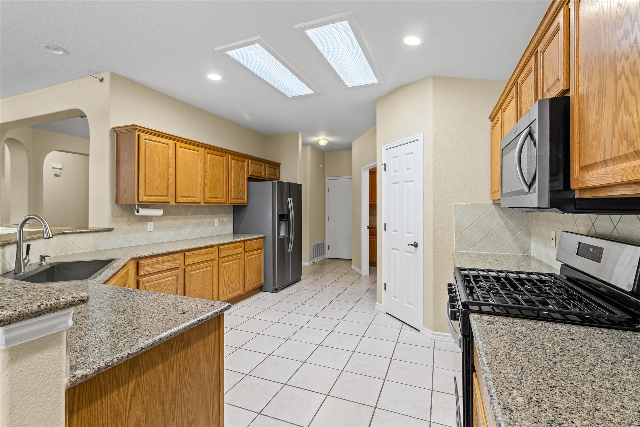 14901 Staked Plains Loop Austin, TX 78717 - Photo 12 of 30 Kitchen featuring backsplash, appliances with stainless steel finishes, brown cabinets, light stone counters, and recessed lighting