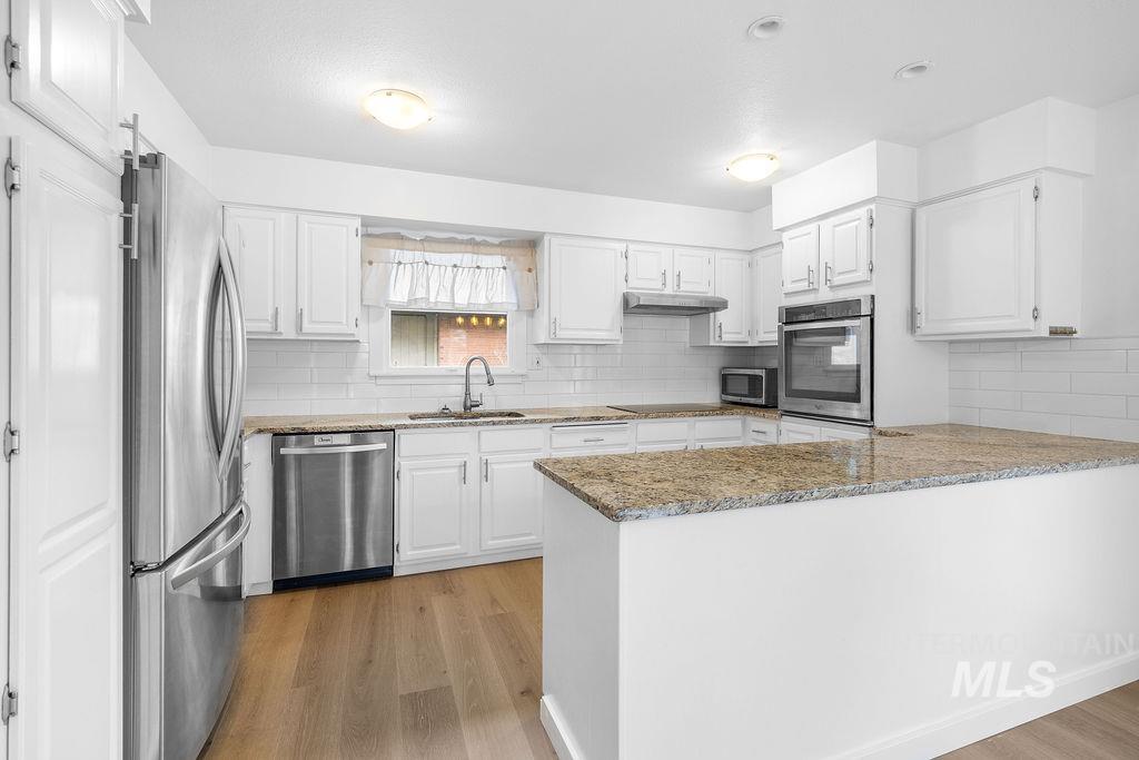 1561 Lenz Lane Boise, ID 83712 - Photo 7 of 29 Kitchen with light stone countertops, a peninsula, stainless steel appliances, and light wood-style flooring