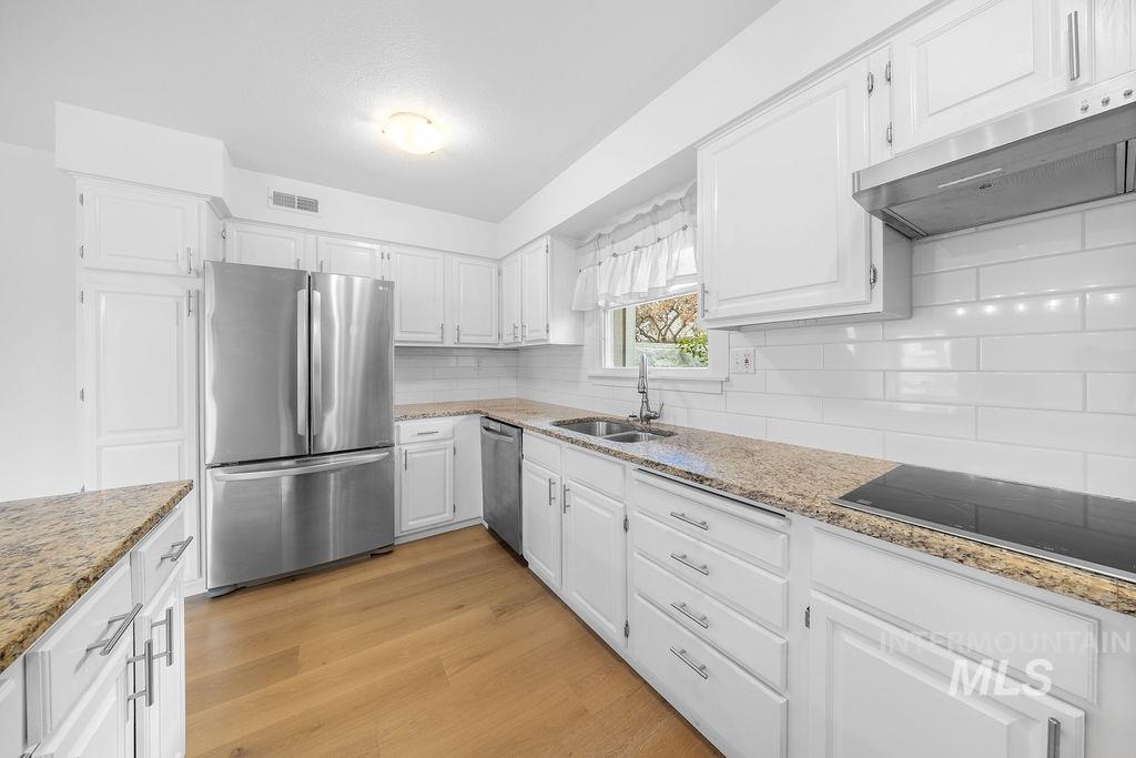 1561 Lenz Lane Boise, ID 83712 - Photo 8 of 29 Kitchen featuring stainless steel appliances, light stone countertops, backsplash, white cabinets, and light wood-style floors
