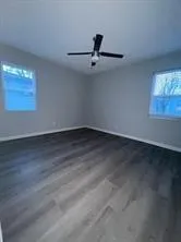 an empty room with wooden floor fan and windows
