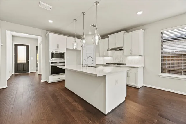 a kitchen with stainless steel appliances kitchen island granite countertop a white stove top oven a sink dishwasher and a refrigerator with wooden floor