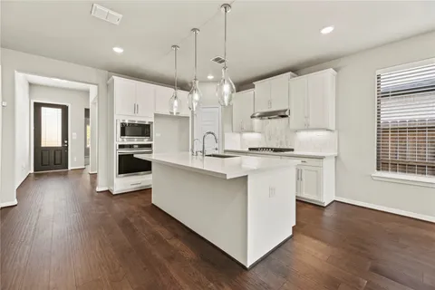 a kitchen with stainless steel appliances kitchen island granite countertop a white stove top oven a sink dishwasher and a refrigerator with wooden floor