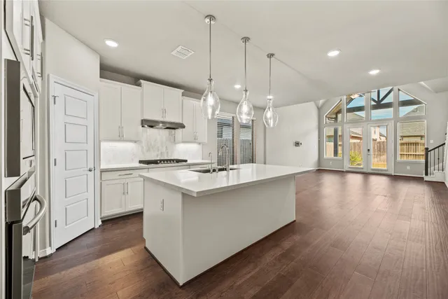 a kitchen with stainless steel appliances kitchen island wooden floors cabinets and a chandelier