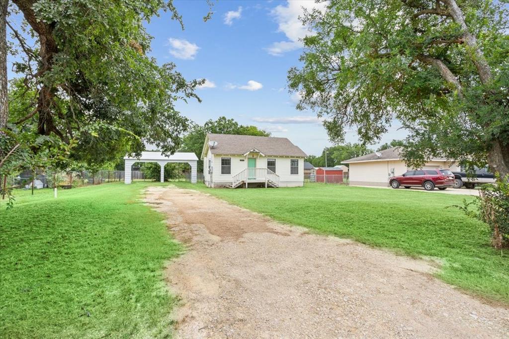 608 9th Street Hico, TX 76457 - Photo 2 of 23 Gravel driveway leading to a white residence with a gabled roof and front porch