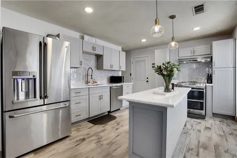 a kitchen with granite countertop a refrigerator oven a sink and white cabinets