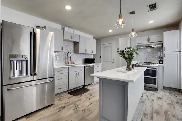 a kitchen with granite countertop a refrigerator oven a sink and white cabinets