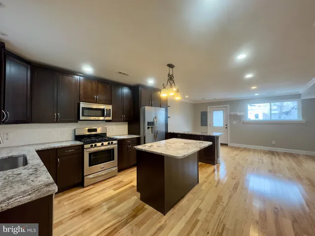 a large kitchen with stainless steel appliances granite countertop a stove a sink dishwasher a refrigerator white cabinets wooden floor and a fireplace