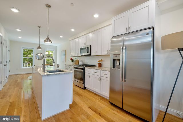 a kitchen with stainless steel appliances granite countertop a refrigerator a oven and a sink with wooden floor