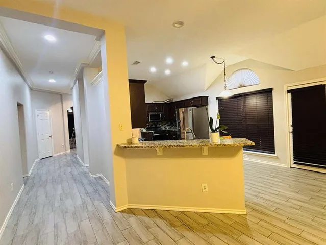 a living room with stainless steel appliances kitchen island granite countertop a refrigerator a stove and a wooden floors