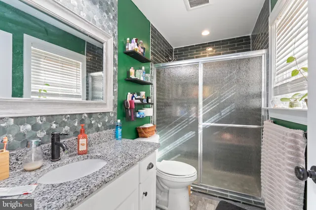 a bathroom with a granite countertop sink a toilet a mirror and shower