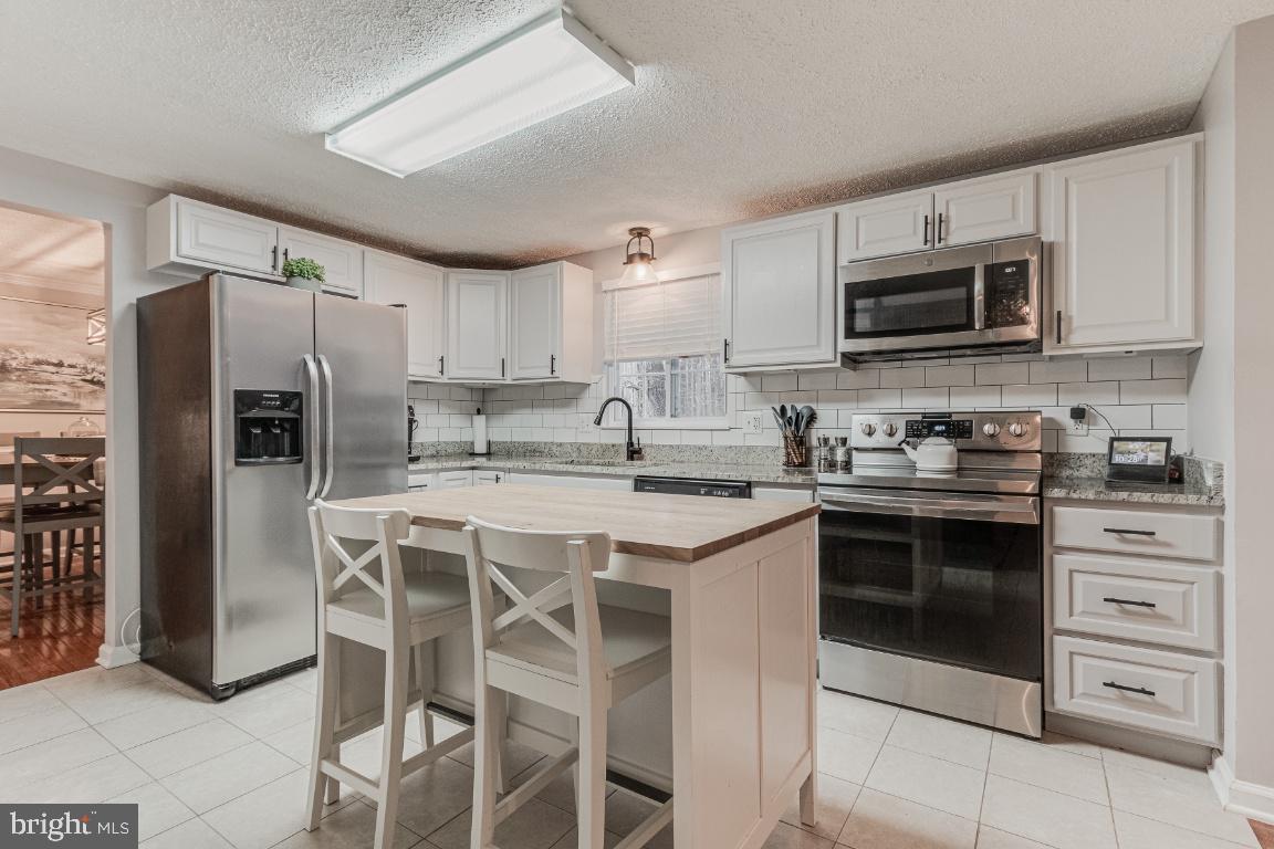 a kitchen with stainless steel appliances granite countertop a stove top oven a refrigerator a sink and chairs