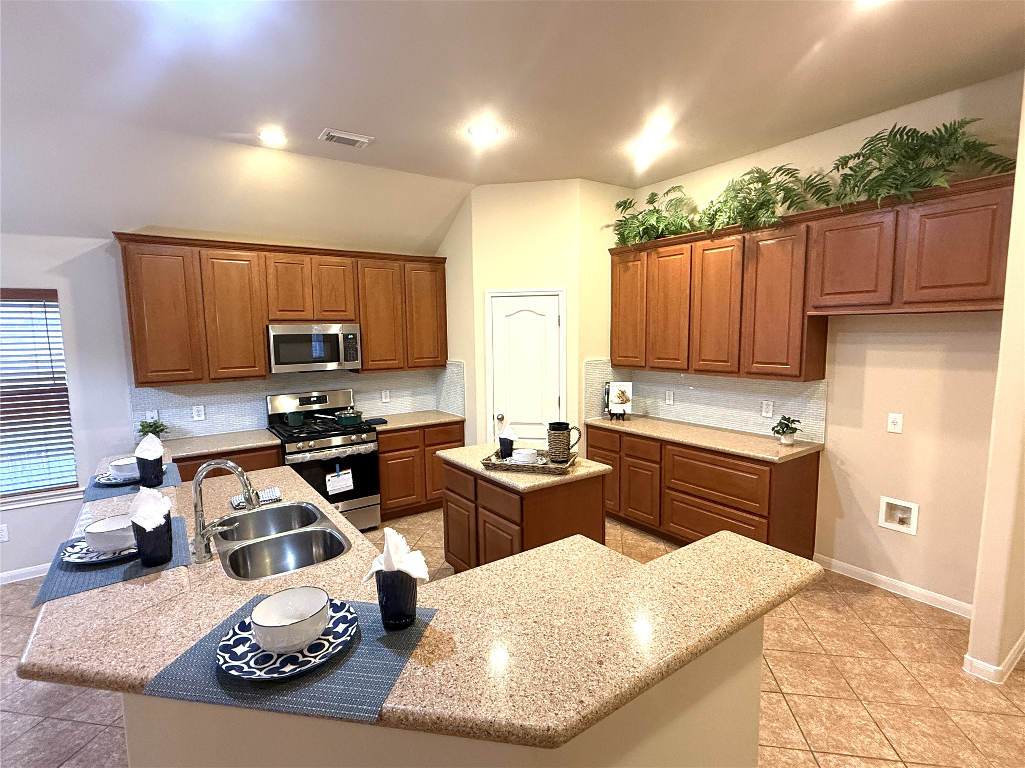 608 Pebblestone Walk Drive Cedar Park, TX 78613 - Photo 8 of 27 Kitchen with wood finish cabinetry, a kitchen island with sink, stainless steel appliances, light tile patterned flooring, and tasteful backsplash
