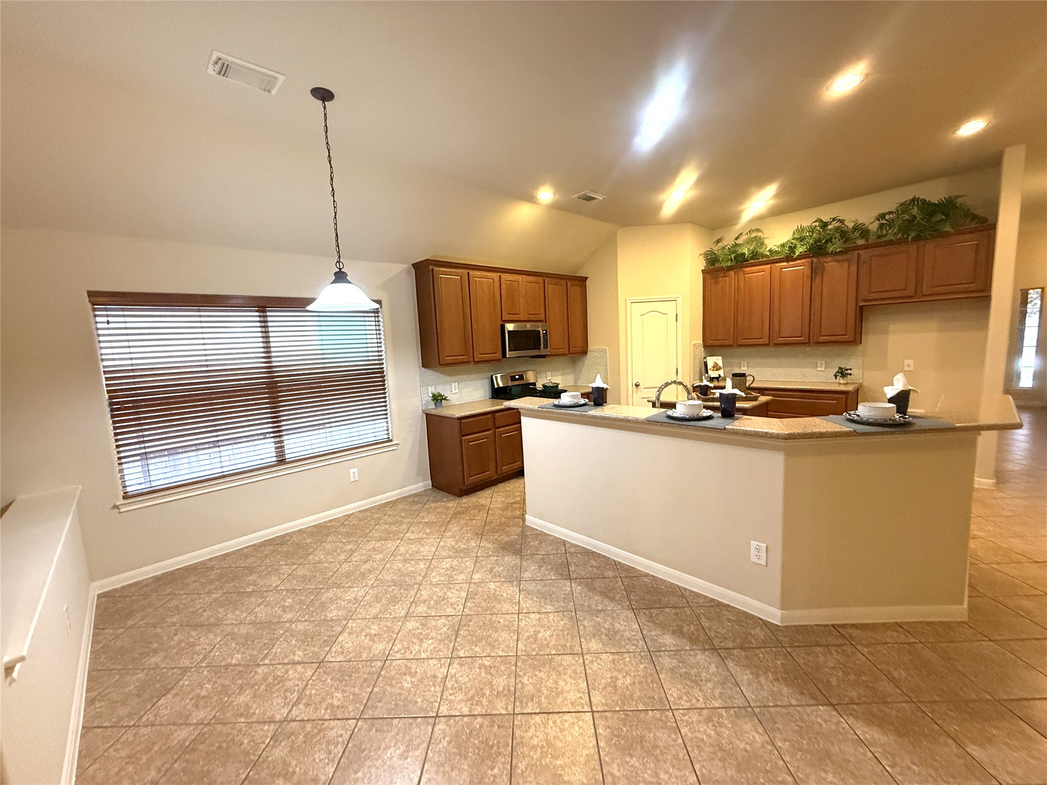 608 Pebblestone Walk Drive Cedar Park, TX 78613 - Photo 9 of 27 Kitchen with wood finish cabinets, a kitchen island with sink, stainless steel appliances, decorative light fixtures, and vaulted ceiling