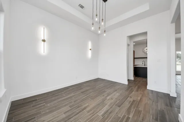 an empty room with wooden floor chandelier and windows