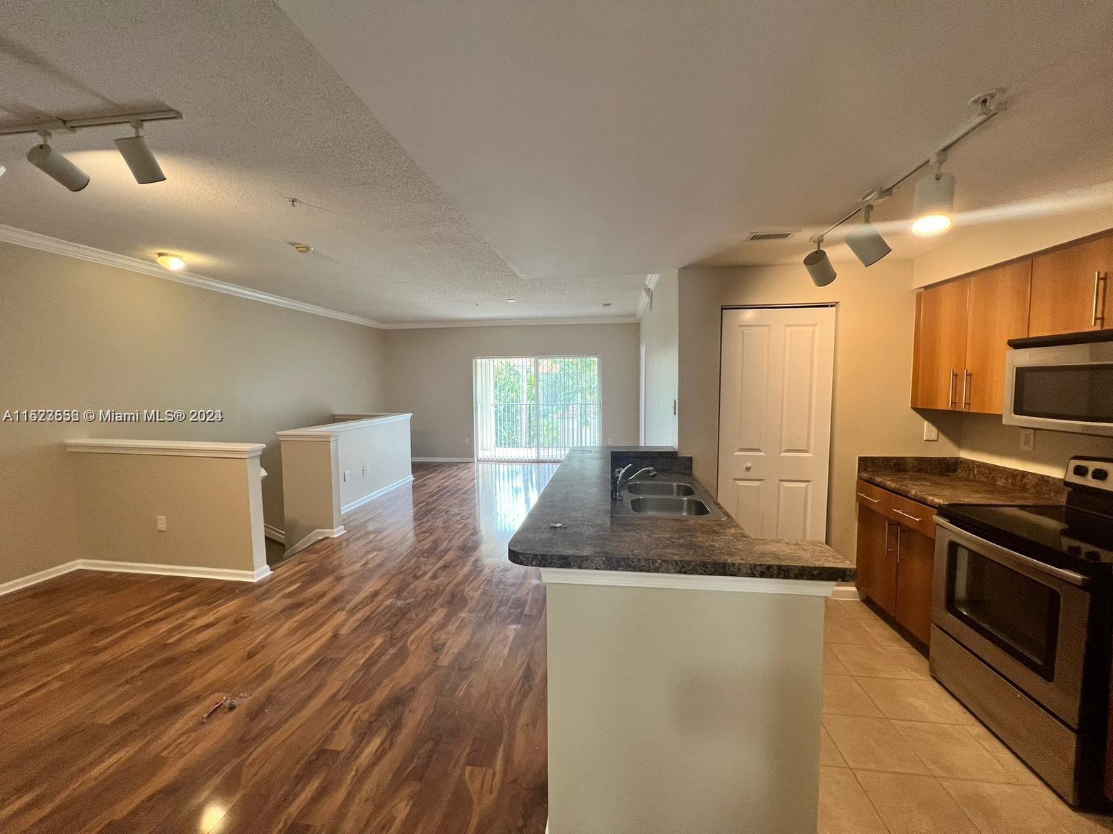 5940 West Sample Road, Unit 304 Coral Springs, FL 33067 - Photo 8 of 18 a kitchen with stainless steel appliances granite countertop a refrigerator a stove and a sink with wooden floor