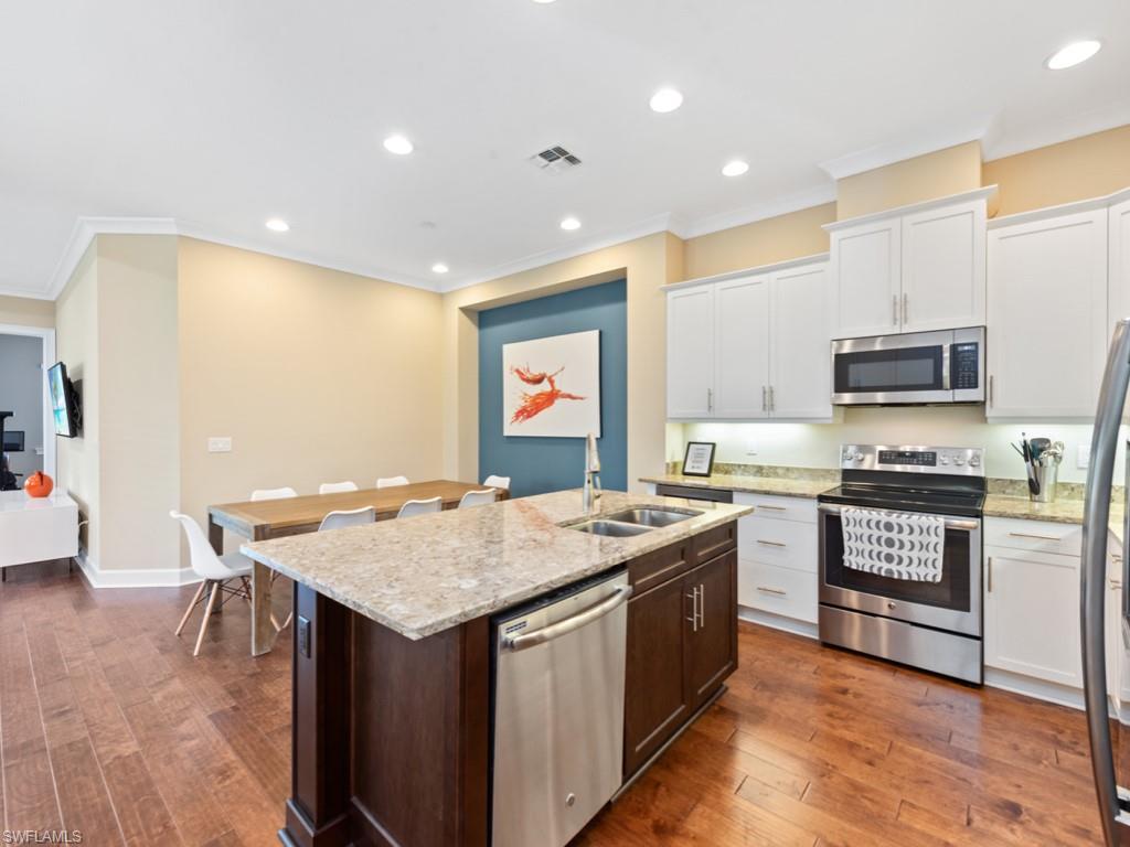 5697 Highbourne Drive Naples, FL 34113 - Photo 11 of 35 a kitchen with stainless steel appliances granite countertop a stove top oven a sink dishwasher and a refrigerator with wooden floor