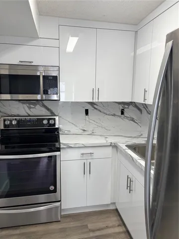 a kitchen with stainless steel appliances granite countertop a refrigerator a sink and white cabinets