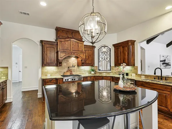 a kitchen with stainless steel appliances granite countertop a sink a stove and chairs with wooden floor