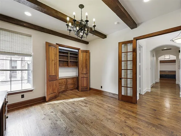 an empty room with wooden floor chandelier and windows